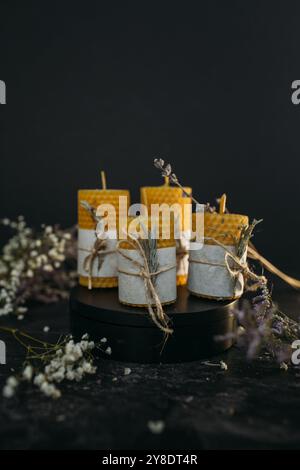 Un gruppo di candele di cera d'api fatte a mano, ciascuna con una struttura a nido d'ape unica, si trova su una superficie scura circondata da fiori secchi e spago. Foto Stock