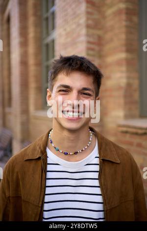 Ritratto di un giovane e bello uomo caucasico felice con un grande sorriso che posa guardando la macchina fotografica all'aperto. Foto Stock