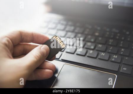 Scheda di memoria in mano, laptop, tastiera. informazioni sull'unità flash. database Foto Stock