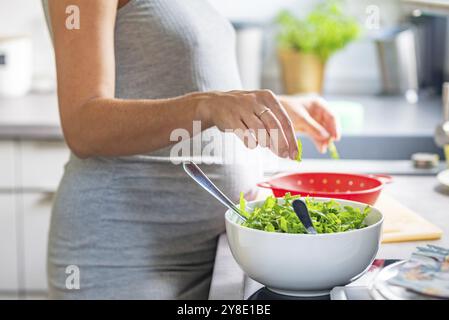 Una donna incinta prepara un pasto sano con ingredienti freschi in cucina Foto Stock