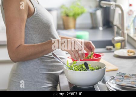 Una donna incinta prepara insalata verde fresca in una cucina moderna Foto Stock