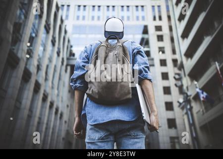 Outdoor ritratto del bel giovane studente maschio con zaino in piedi alla costruzione di sfondo sulla strada mentre aspetta i suoi colleghi. Imprenditore Foto Stock