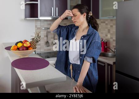 Una donna che soffre di mal di testa in cucina a casa Foto Stock