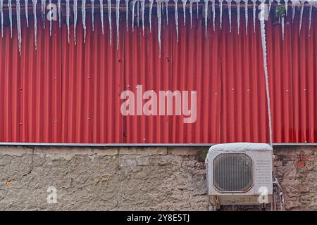 Condizionatore d'aria congelato ghiaccio pericoloso appeso al tetto dell'edificio freddo inverno Foto Stock