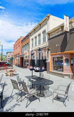 Tavolo e sedie sul patio con ombrelloni sul marciapiede pedonale prima delle vetrine in mattoni dell'inizio del XX secolo del centro di Rifle Colorado - maggio 2024 Foto Stock