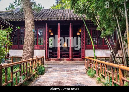 Un tradizionale edificio Cinese con porte di legno rosse sorge in un lussureggiante giardino a Suzhou Foto Stock