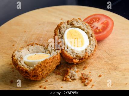 Preparato in modo semplice e pronto da mangiare, con pomodoro fresco a fette, su un tagliere di legno con briciole di pane sciolte che cadono sulla superficie di legno. Foto Stock