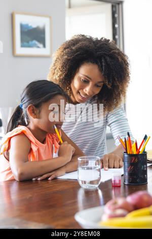 La donna birazziale aiuta sua figlia con i compiti a casa Foto Stock