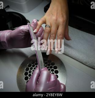 L'estetista sta depositando le unghie del suo cliente che sta facendo una manicure in un salone di bellezza. Foto Stock