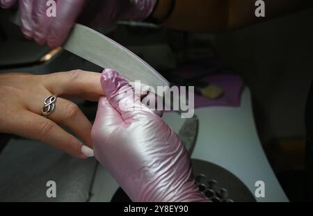 L'estetista sta depositando le unghie del suo cliente che sta facendo una manicure in un salone di bellezza. Foto Stock