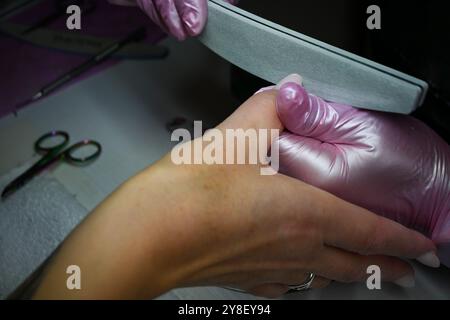 L'estetista sta depositando le unghie del suo cliente che sta facendo una manicure in un salone di bellezza. Foto Stock