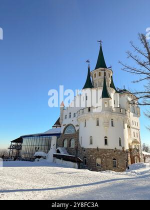 Il bellissimo castello bianco della principessa si erge maestosamente su un paesaggio innevato sotto un cielo azzurro. Design architettonico e ambientazione invernale Foto Stock