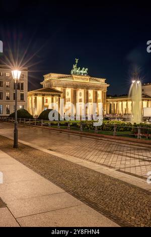 La porta di Brandeburgo illuminata di Berlino con una fontana di notte Foto Stock