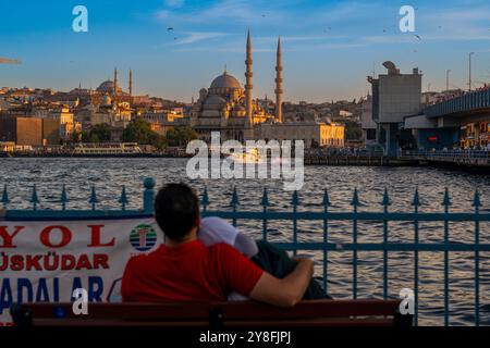 Turkiye. Istanbul. Una coppia seduta su una panchina gode del tramonto sul Bosforo, con una vista della magnifica Moschea Yeni Camii Foto Stock