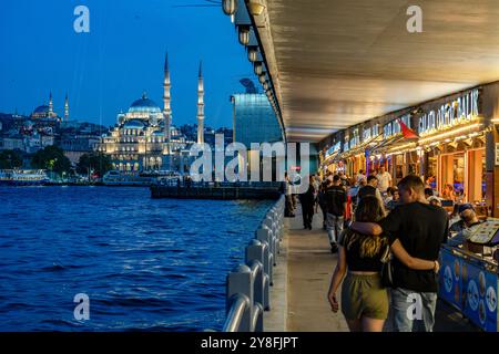 Turkiye. Istanbul. Scena notturna sul ponte Galata, con vivaci ristoranti sulla destra e la moschea Yeni illuminata sullo sfondo Foto Stock