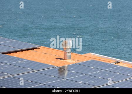 Il camino metallico con ventilatore a turbina è installato su un tetto con pannelli solari vicino al mare Foto Stock