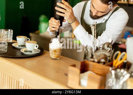 Un barista dedicato decora elegantemente un caffè da dessert con panna montata, mostrando la sua arte in una vivace caffetteria piena di luce calda e invit Foto Stock