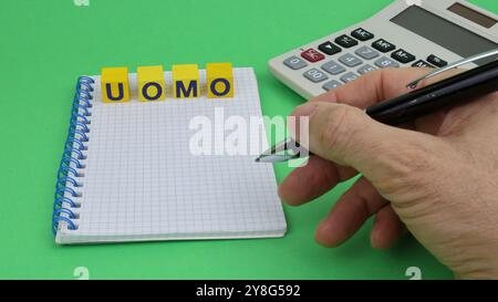 L'UOMO del mondo in italiano scritto su cubi di legno. Qualcuno inserisce la scrittura con una scrittura a mano sul blocco note e uno spazio Copia sfondo verde Foto Stock