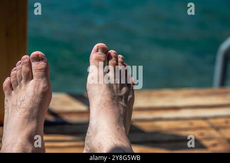 Uno scatto ravvicinato di dita e piedi di un uomo che riposano nella sabbia calda vicino al mare, catturando l'essenza del relax e dello stile di vita in spiaggia. Foto Stock