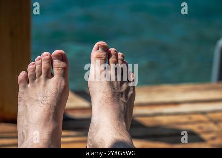 Uno scatto ravvicinato di dita e piedi di un uomo che riposano nella sabbia calda vicino al mare, catturando l'essenza del relax e dello stile di vita in spiaggia. Foto Stock