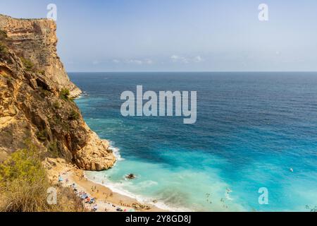 Questa immagine mostra uno splendido paesaggio costiero caratterizzato da un'alta scogliera sul lato sinistro che si affaccia su un mare cristallino e turchese. Foto Stock