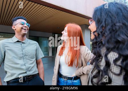 Gruppo di giovani colleghi che ridono e condividono fuori dall'edificio dell'ufficio dopo una giornata lavorativa produttiva Foto Stock