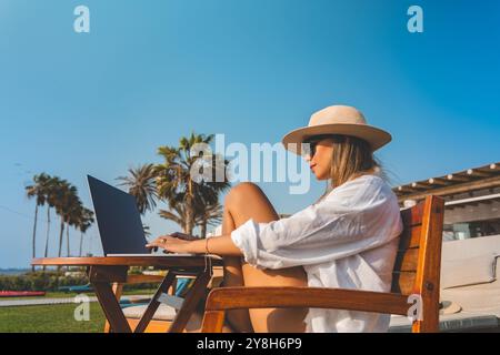 Donna che lavora a distanza con Ocean View. la donna è seduta su una sedia di legno con un portatile davanti a sé Foto Stock