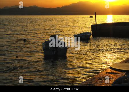 Le barche da pesca si arrampicano sulle onde del Mar Ionio al tramonto. Il sole tramonta le montagne, il mare e la passeggiata dorati. Serata estiva a Loutraki, Foto Stock