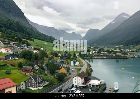 Alusund, Norvegia 15 agosto 2024 - Un fiordo panoramico circondato da torreggianti montagne, con un affascinante villaggio lungo la sua riva. Lussureggianti campi verdi Foto Stock