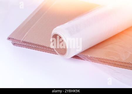 Vista dall'alto su pellicola estensibile e cartone su sfondo bianco. Imballaggio delle merci. Un coltello per tagliare il cartone.. Foto Stock