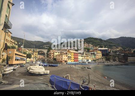 Baia con una spiaggia e barche coperte di fronte a una città iitaliana su una scogliera in una giornata nuvolosa Foto Stock