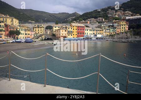 Baia con una spiaggia e barche coperte di fronte a una città iitaliana su una scogliera in una giornata nuvolosa Foto Stock