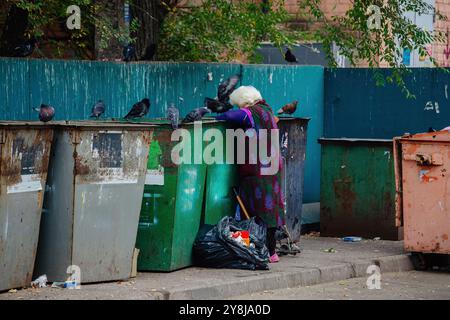 Una vecchia senzatetto che guarda nella scatola della spazzatura in cerca di cibo. Concetto di problema dei senzatetto. Foto Stock