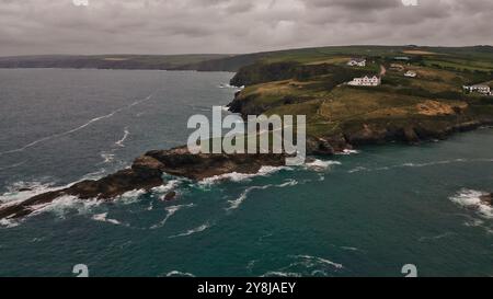 Una vista panoramica sulla costa caratterizzata da scogliere aspre, colline verdi ondulate e case bianche lungo la costa. Le onde oceaniche si schiantano contro l'uscita rocciosa Foto Stock