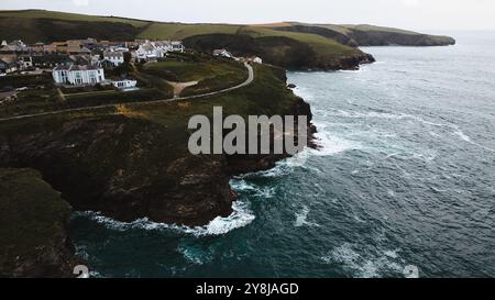 Una vista panoramica della costa caratterizzata da un piccolo villaggio arroccato su una scogliera che si affaccia sull'oceano. Le onde si infrangono contro la costa rocciosa, con un lussureggiante hil verde Foto Stock