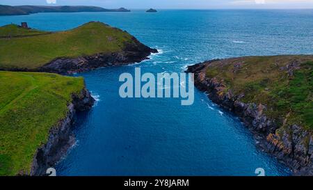 Vista aerea di un tranquillo paesaggio costiero caratterizzato da lussureggianti colline verdi e un mare blu calmo. L'acqua scorre tra due formazioni rocciose, con i distante Foto Stock