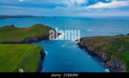 Vista aerea di un tranquillo paesaggio costiero caratterizzato da verdi colline, coste rocciose e un mare blu calmo. L'orizzonte è punteggiato di piccole isole sotto un c Foto Stock