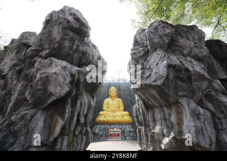 La grande statua dorata del Buddha con cascata e muro di pietra sullo sfondo a Wat Lak si Rat Samoson, Samut Sakhon, Thailandia. Foto Stock