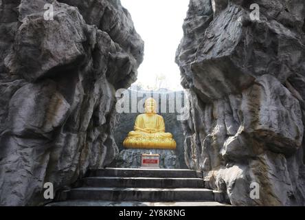 La grande statua dorata del Buddha con cascata e muro di pietra sullo sfondo a Wat Lak si Rat Samoson, Samut Sakhon, Thailandia. Foto Stock