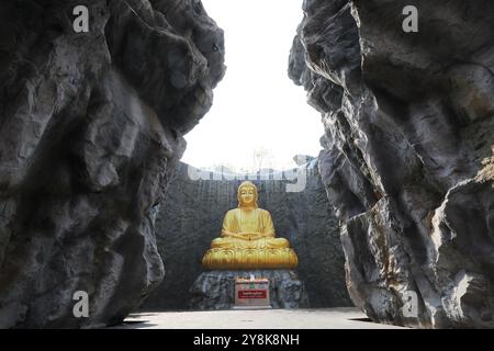 La grande statua dorata del Buddha con cascata e muro di pietra sullo sfondo a Wat Lak si Rat Samoson, Samut Sakhon, Thailandia. Foto Stock