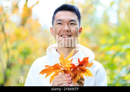 Un giovane tiene in mano un mazzo di foglie d'acero autunnale colorate in un parco forestale all'aperto Foto Stock