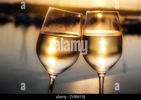 Due bicchieri di vino tostato al tramonto sulla riva di fronte all'acqua calma, romanticismo in una splendida serata estiva durante le vacanze, copia spazio, se Foto Stock