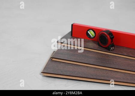 Metro a nastro, livella e pezzi per pavimenti in laminato su superficie ruvida grigia, primo piano Foto Stock