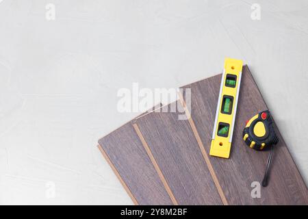 Diversi strumenti di misurazione e pezzi di pavimentazione in laminato su superficie ruvida grigia. vista dall'alto. Spazio per il testo Foto Stock