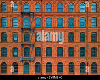 Facciata simmetrica di uno storico edificio industriale in mattoni rossi a Łódź, Polonia, con più finestre ad arco e una scalinata esterna Foto Stock