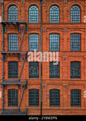 Facciata simmetrica di uno storico edificio industriale in mattoni rossi a Łódź, Polonia, con più finestre ad arco e una scalinata esterna Foto Stock