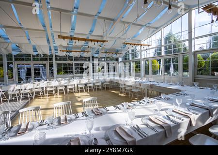 Una luminosa sala banchetti con pareti in vetro con tavoli coperti da tovaglie bianche. Stoviglie pronte per servire piatti. Foto scattata durante il giorno, con il sole Foto Stock