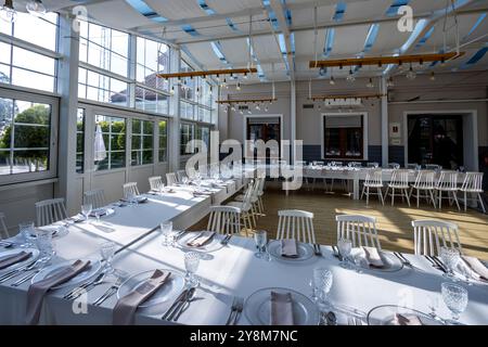 Una luminosa sala banchetti con pareti in vetro con tavoli coperti da tovaglie bianche. Stoviglie pronte per servire piatti. Foto scattata durante il giorno, con il sole Foto Stock