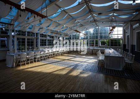 Una luminosa sala banchetti con pareti in vetro con tavoli coperti da tovaglie bianche. Stoviglie pronte per servire piatti. Foto scattata durante il giorno, con il sole Foto Stock