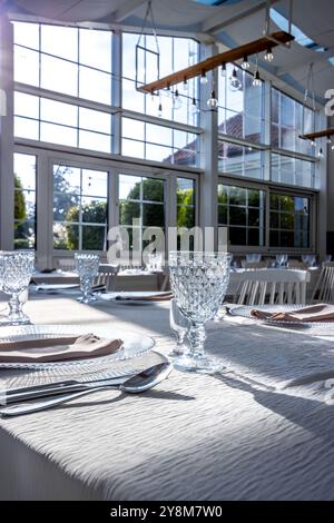 Vetro di cristallo sul tavolo in una luminosa sala banchetti con pareti in vetro. Foto scattate durante il giorno, con la luce del sole che scorre. Foto Stock